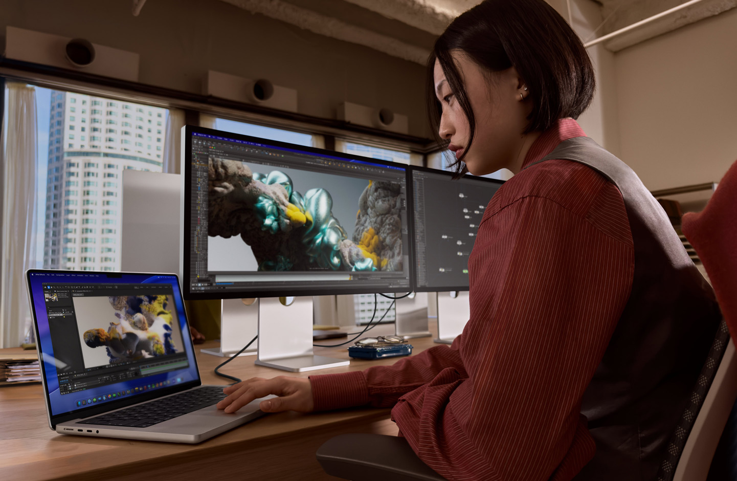 Une personne dans un bureau travaillant sur un MacBook connecté à un Studio Display XDR via un port Thunderbolt 5