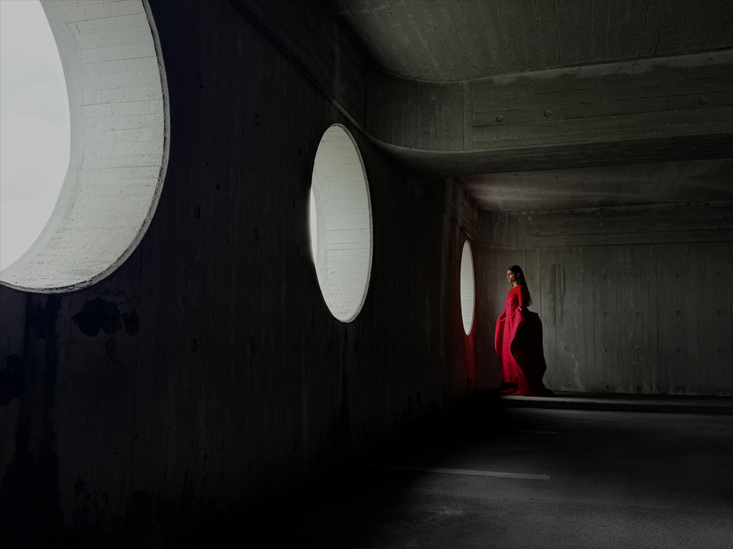 Uma mulher com um longo vestido vermelho a ser fotografada numa sala vazia. A app Fotografia muda de distância focal para ilustrar as capacidades do sistema de câmaras Pro, a mostrar a opção de 35 mm